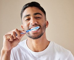 Man smiling while brushing his teeth